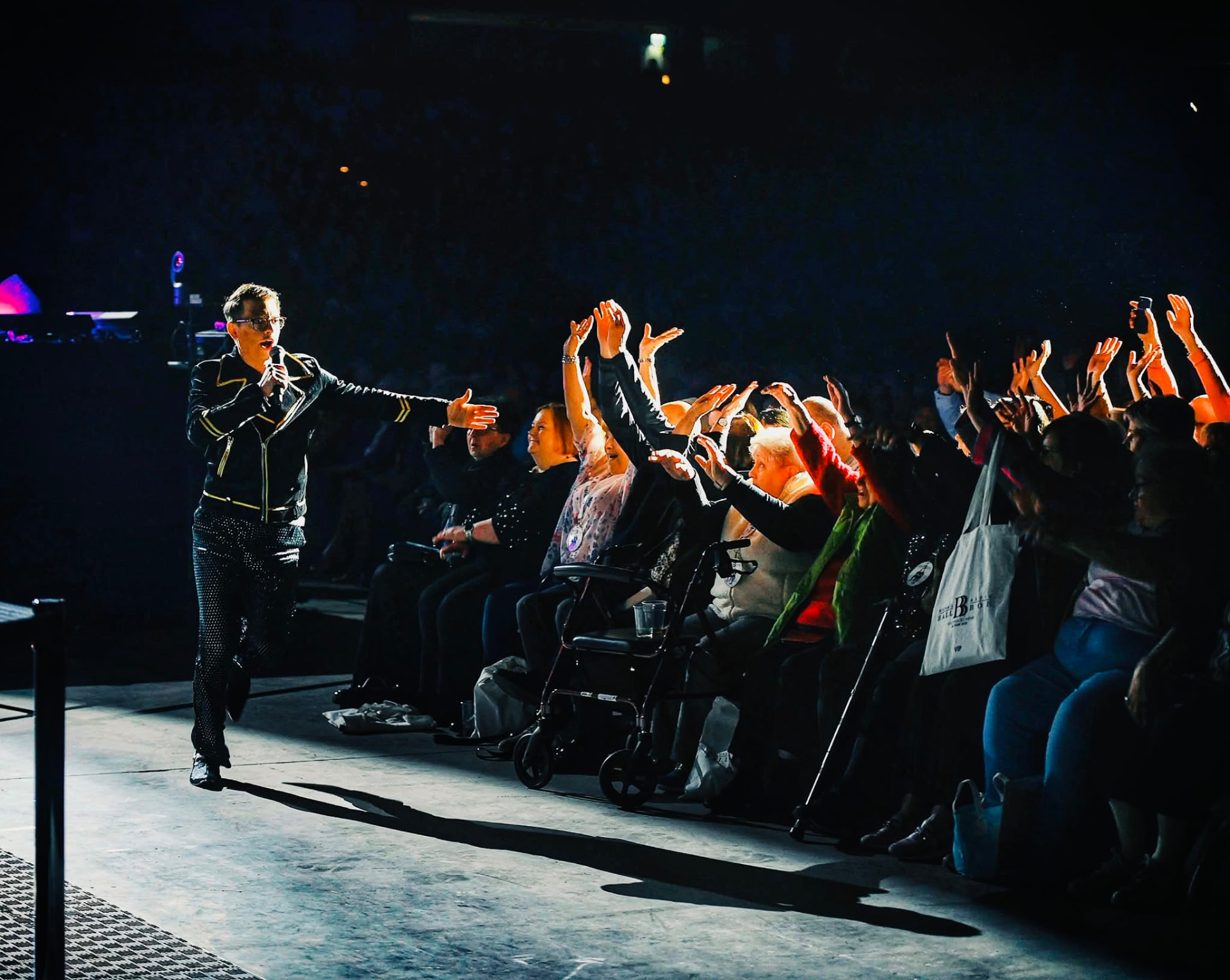 Matthew Pomeroy performing at the edge of an arena stage, microphone in hand, as the front row reaches up towards him